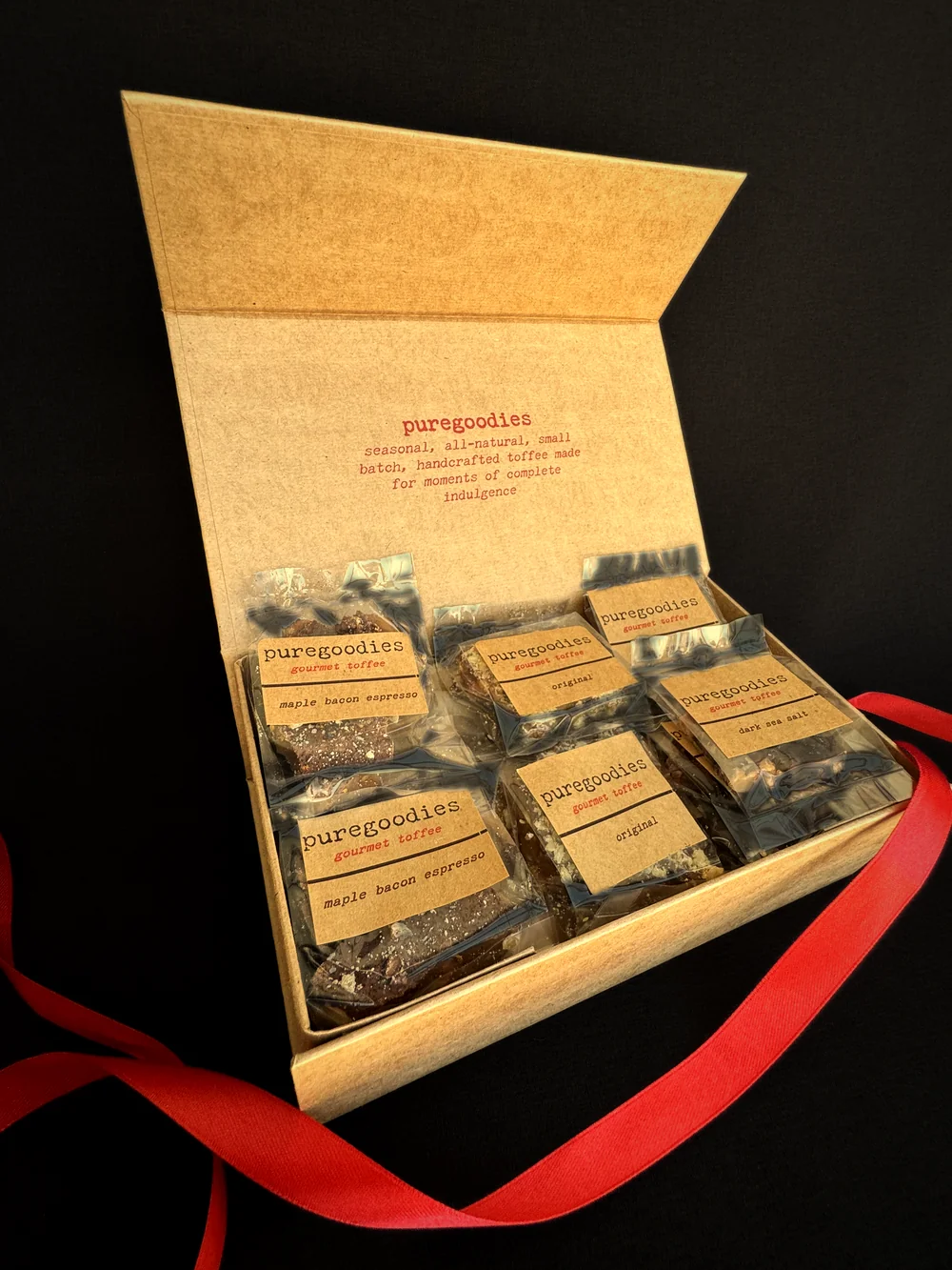 An open puregoodies box of six wrapped toffee pieces in three flavors, under the printed lid message